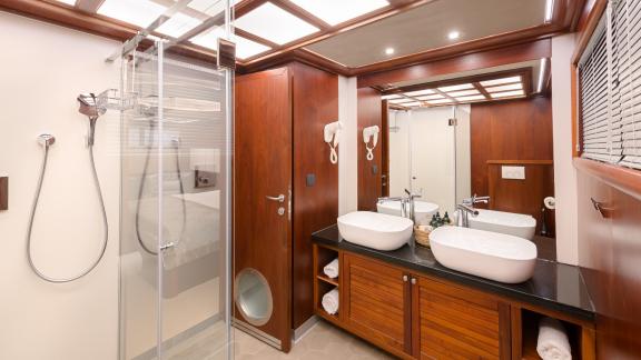Bathroom with shower, double washbasin, mirror and wooden cabinets in the Lady Gita's master stateroom.